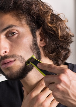 Close up photo of a man using a Philips OneBlade male grooming tool to shape his beard