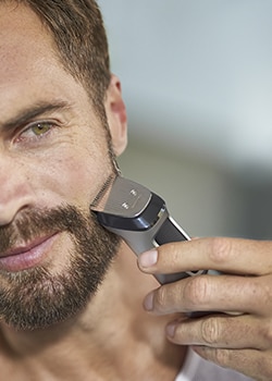 Close up photograph of a man using a men’s multi groomer to trim his beard